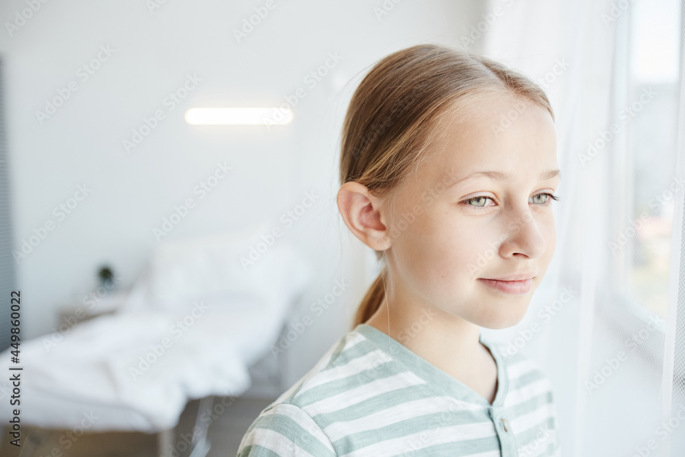 Minimal portrait of smiling girl looking at window in white hospital room, copy space Minimal portrait of smiling girl looking at window in white hospital room, copy space