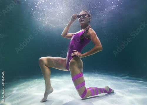 beautiful girl in a lilac swimsuit sits and sunglasses underwater in the pool on a blue background © Pavel Karchevskii