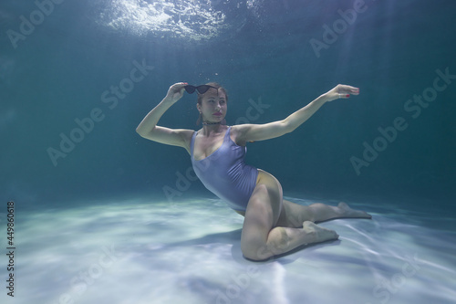 fashion model posing underwater in the pool in a silver swimsuit and sunglasses