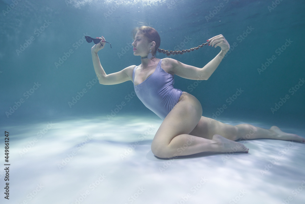 fashion model posing underwater in the pool in a silver swimsuit and sunglasses