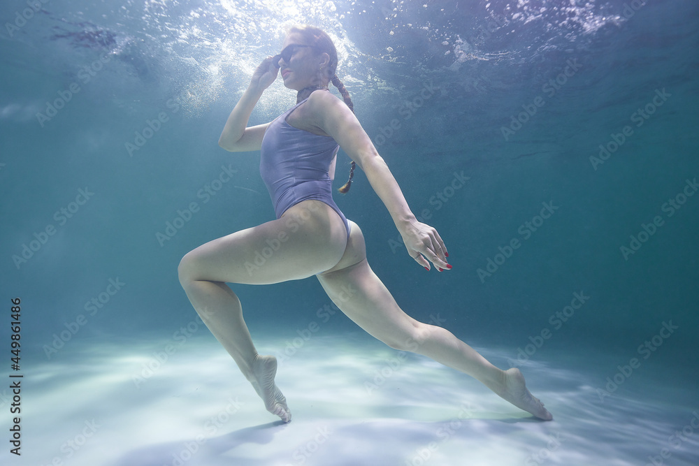 freediver girl dives underwater in the pool in a silver swimsuit and sunglasses on a background of waves