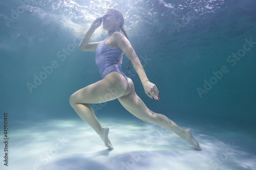 freediver girl dives underwater in the pool in a silver swimsuit and sunglasses on a background of waves photo