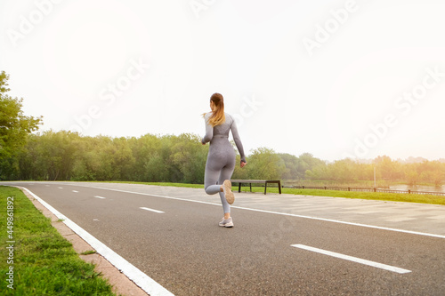 Woman dressed leggings and top running asphalt road summer park. Healthy lifestyle concept. Active and athletic female exercises