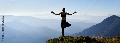 Back view of sporty woman standing on one leg while practicing yoga outdoors in the morning. Panoramic view