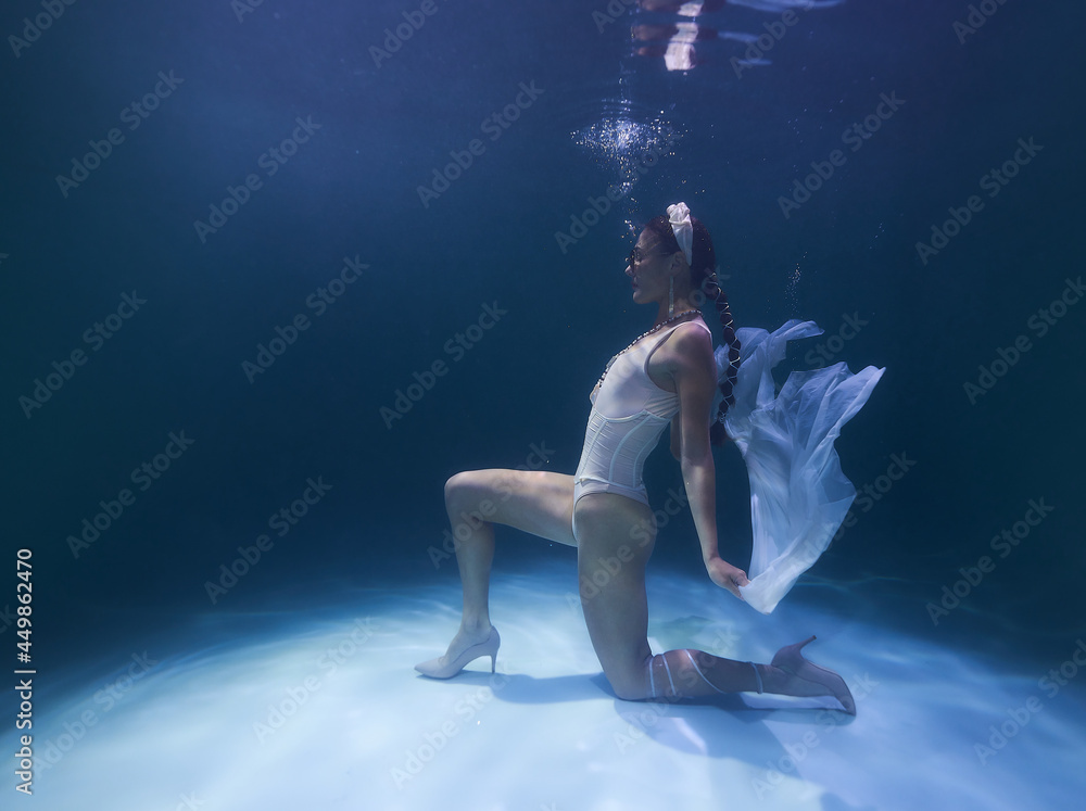 girl in a headdress at the bottom of the pool releases air bubbles