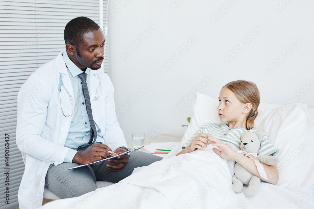 Portrait of young African-American doctor talking to little girl lying in hospital bed, copy space Portrait of young African-American doctor talking to little girl lying in hospital bed, copy space