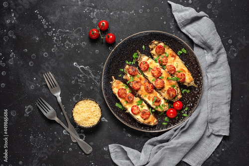 Baked eggplants with cherry tomato and cheese on a black stone background. Top view, flat lay, copy space.
