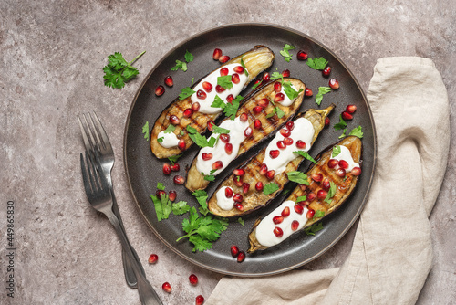Grilled eggplants with yogurt sauce and pomegranate on a brown grunge background. Top view, flat lay