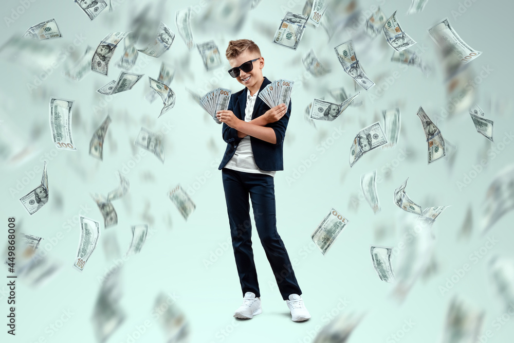 A cute, rich boy with glasses holds dollars and knows how to make money against the background of falling banknotes. Money rain, Financial education, young millionaire, investments, loans, winnings A cute, rich boy with glasses holds dollars and knows how to make money against the background of falling banknotes. Money rain, Financial education, young millionaire, investments, loans, winnings