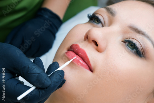 permanent makeup on her lips at the beautician salon. Applying liquid glass to lips