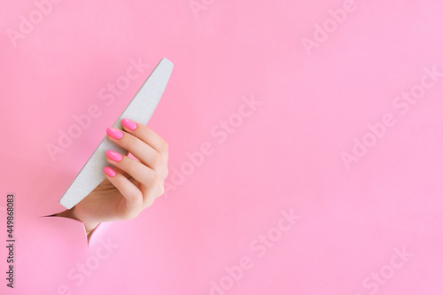 nail file in the hand of a young woman on a pink background from the hole.
