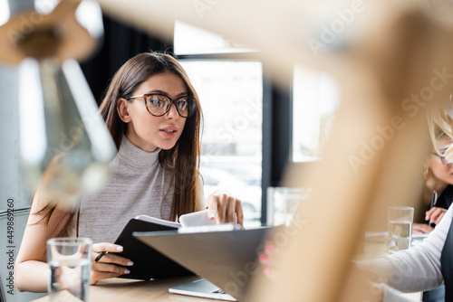 brunette businesswoman in eyeglasses working with documents on blurred foreground