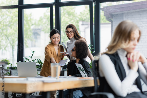 positive multiethnic businesswomen talking near window in office on blurred foreground © LIGHTFIELD STUDIOS