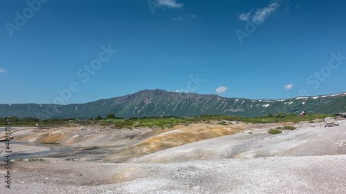 A river of hot springs flows in the caldera of an extinct volcano. There are deposits of sulfur and minerals on the earth. A mountain range against the blue sky. Kamchatka. Uzon