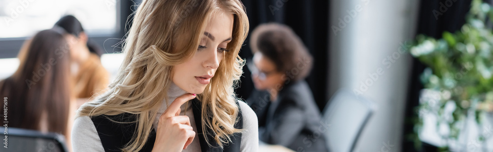 pensive businesswoman touching chin near multiethnic colleagues on blurred background, banner pensive businesswoman touching chin near multiethnic colleagues on blurred background, banner