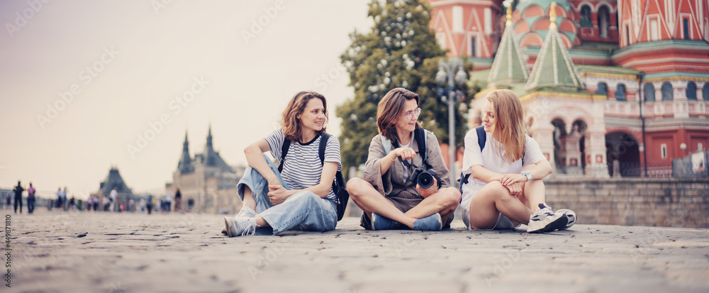 Three beautiful young woman friends sitting on paving stones while traveling in Moscow on Red Square