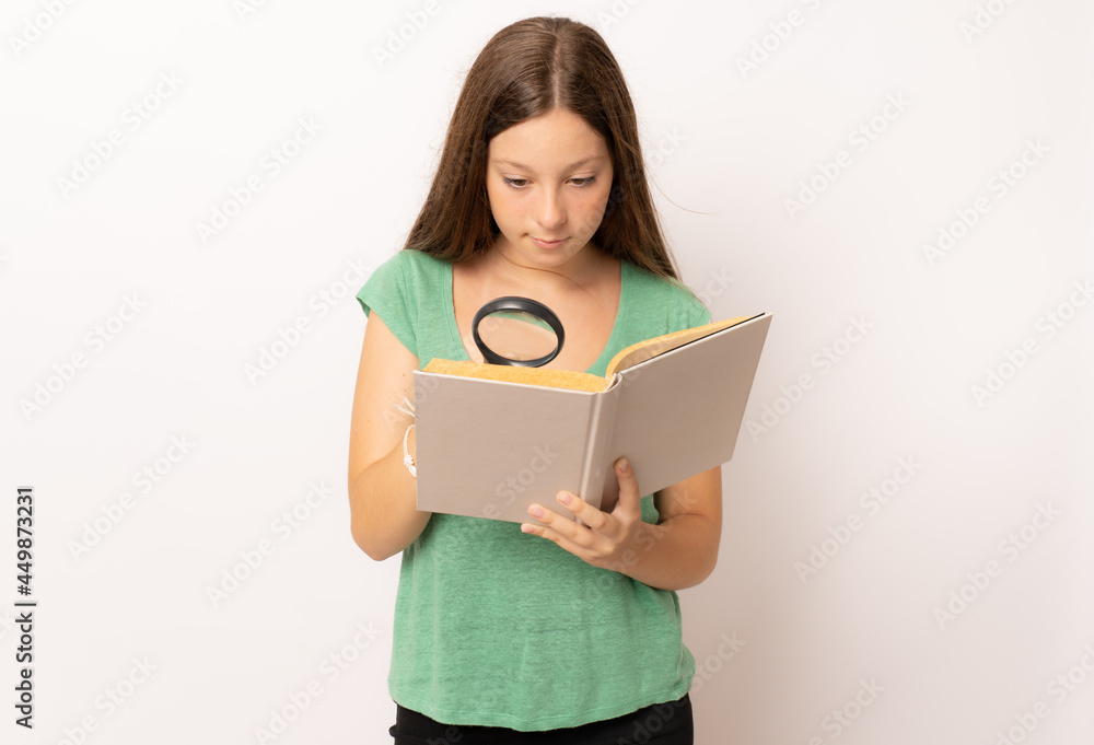 Young girl holding a book looking through a magnifying glass over white background. Young girl holding a book looking through a magnifying glass over white background.