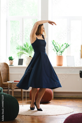 Lovely woman wearing a long navy dress and high hills shoes having fun at home dancing, smiling. She happily celebrates success photo