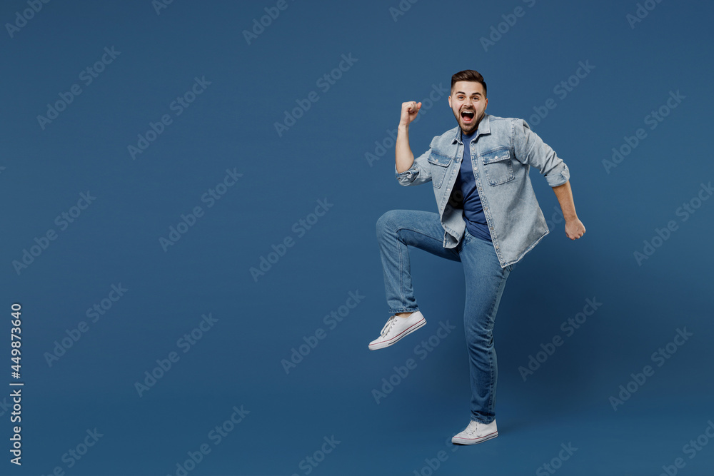 Full size length body laughing beautiful young brunet man 20s mouth open wears denim jacket doing winner gesture celebrating clenching fists say yes isolated on dark blue background studio portrait