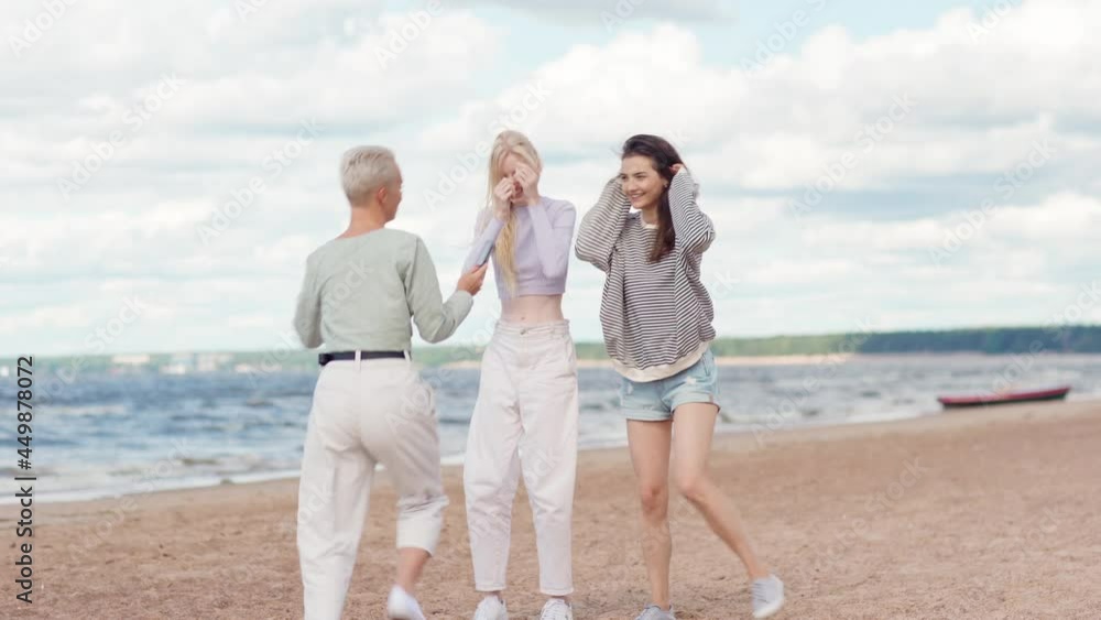 Group of young female friends having fun shooting short dance video for social media on sea beach. Woman filming girlfriends with smartphone and showing footage to them Group of young female friends having fun shooting short dance video for social media on sea beach. Woman filming girlfriends with smartphone and showing footage to them