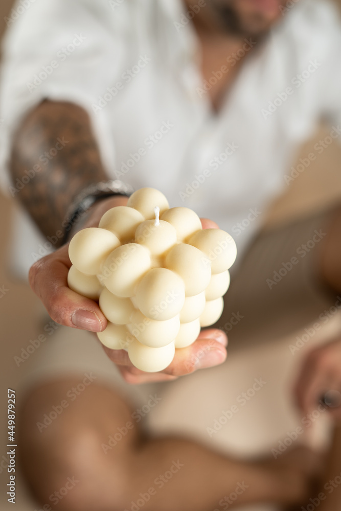 A male hand showing an off-white bubble candle into the camera A male hand showing an off-white bubble candle into the camera