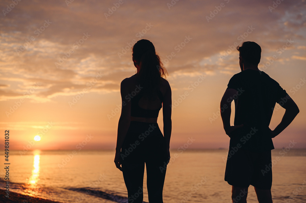 Back view couple young two friend sporty sportswoman sportsman woman man in sport clothes warm up training stand akimbo on sunrise over sea ocean beach outdoor jog on seaside in summer day morning