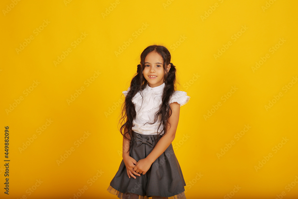 Naklejka premium a beautiful happy dark-skinned schoolgirl girl with dark hair in a school uniform, a gray skirt and a white blouse