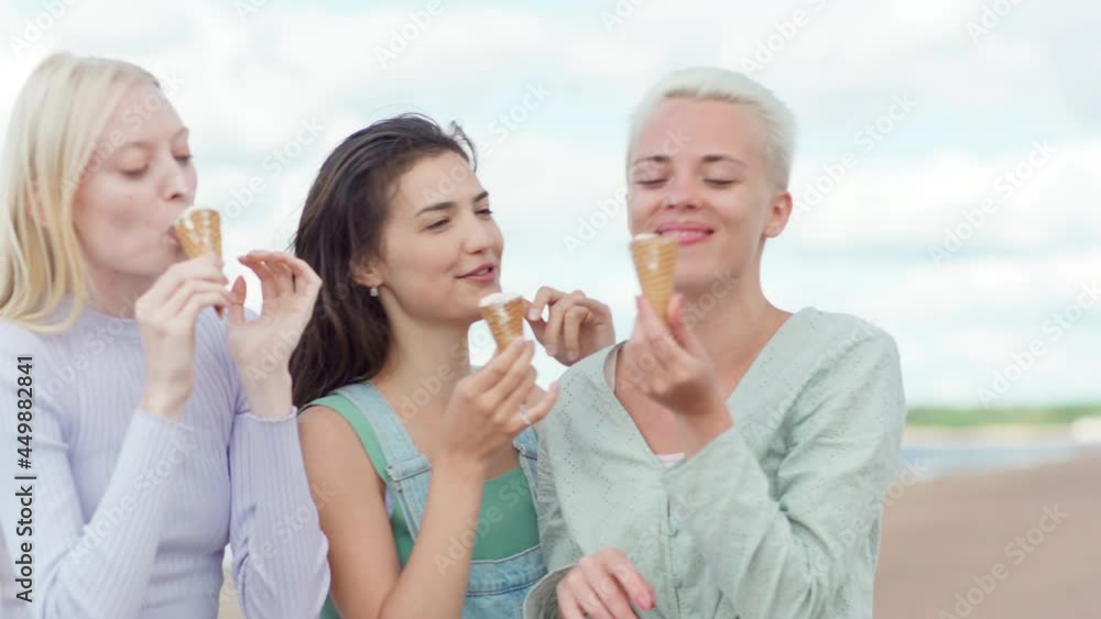 Group of three girlfriends enjoying eating ice cream in cones and having fun smudging each others noses. Loving female friends spending leisure time together on beach Group of three girlfriends enjoying eating ice cream in cones and having fun smudging each others noses. Loving female friends spending leisure time together on beach