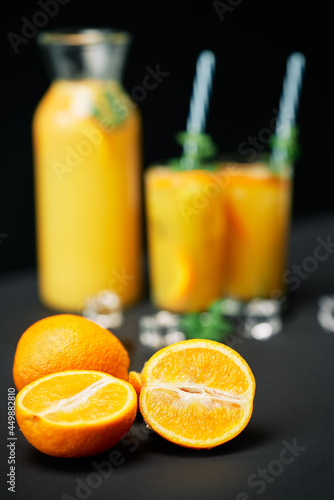 Delicious fresh orange juice with ice, mint and fruits on black table background.