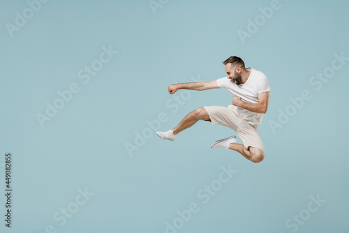 Full length young strong fighter caucasian man 20s in casual white t-shirt jump high do fighting gesture isolated on plain pastel light blue color background studio portrait. People lifestyle gesture. © ViDi Studio