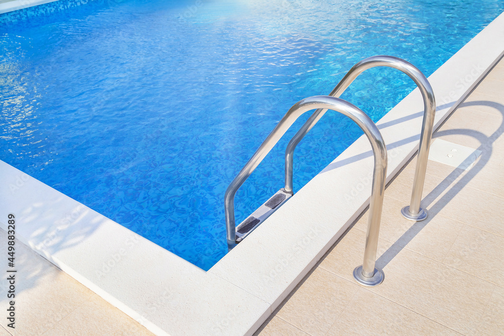Close up of ladder stainless handrails (stairs) into the blue swimming pool. Vacation and sport concept.