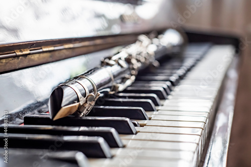 A fully assembled clarinet rests on an old piano by a sunny window.