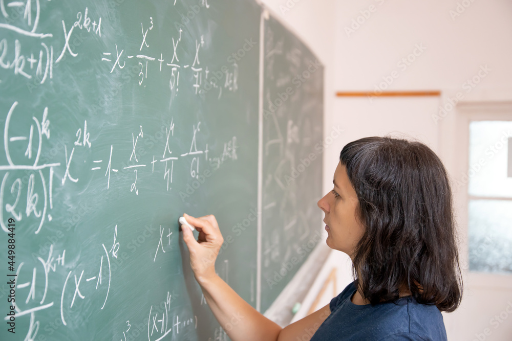 Female student or teacher in the classroom writing on chalkboard mathematical equations Female student or teacher in the classroom writing on chalkboard mathematical equations