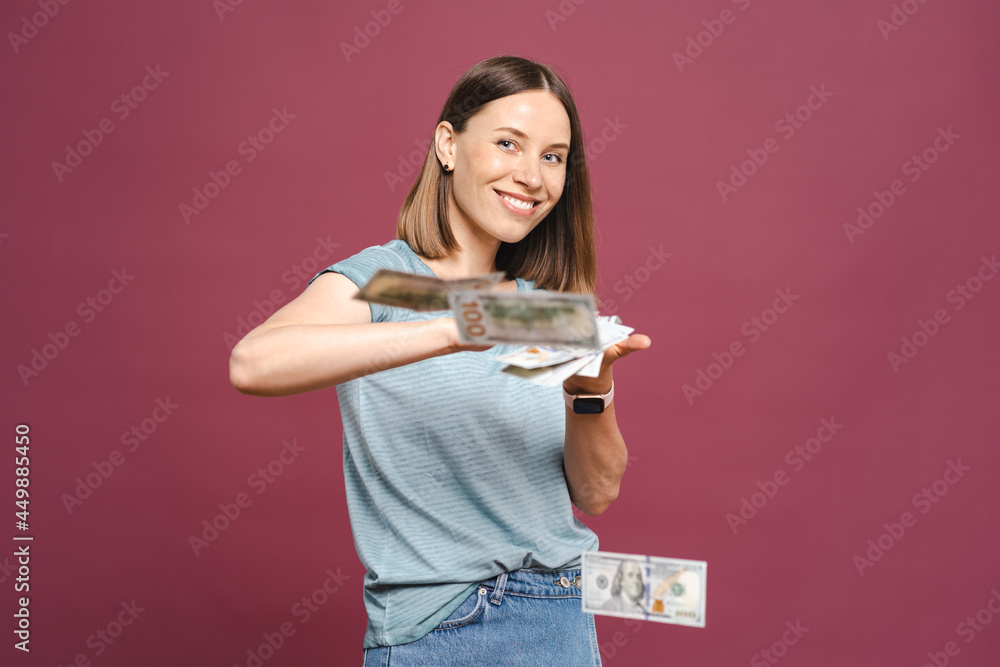 Photo of a surprised young girl reacting excited to flying money over a pink background, making a winner gesture with copy space Photo of a surprised young girl reacting excited to flying money over a pink background, making a winner gesture with copy space
