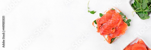 Toast with salted trout, curd cheese and arugula on the white table. Web banner with copy space