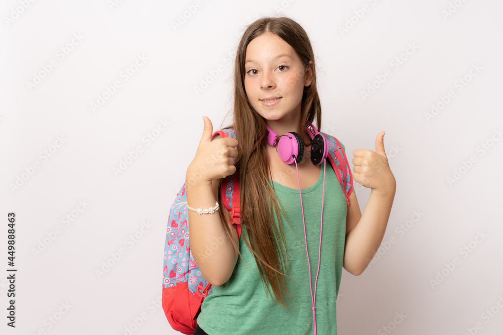 Portrait of a smiling female teenager with backpack and headphones with thumbs up isolated on a white background Portrait of a smiling female teenager with backpack and headphones with thumbs up isolated on a white background