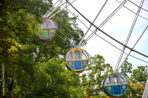 Three cabins of the Ferris wheel in the midst of green trees and against the backdrop of a blue ned with clouds. photo