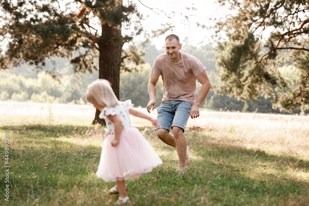Fototapeta premium Father is playing with little daughter on summer day. Portrait dad with child together. Daddy, little daughter outdoors. Young father with baby girl walk in park. Family holiday in garden or forest.