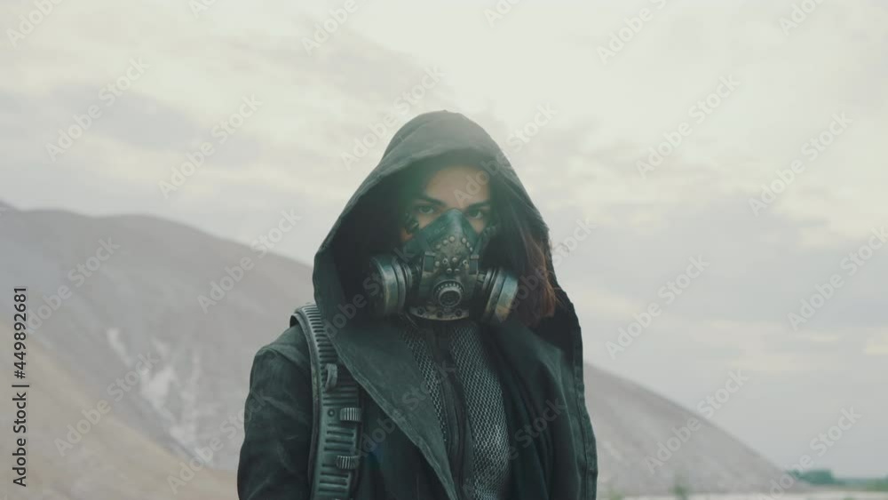Portrait woman in grunge clothes hooded mantle and protective gas mask posing by white hills looking into camera. Future female survivor. Post apocalyptic world. Steadicam following shot Portrait woman in grunge clothes hooded mantle and protective gas mask posing by white hills looking into camera. Future female survivor. Post apocalyptic world. Steadicam following shot