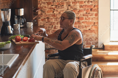 Valokuva Side view portrait of contemporary tattooed woman with disability cooking dinner