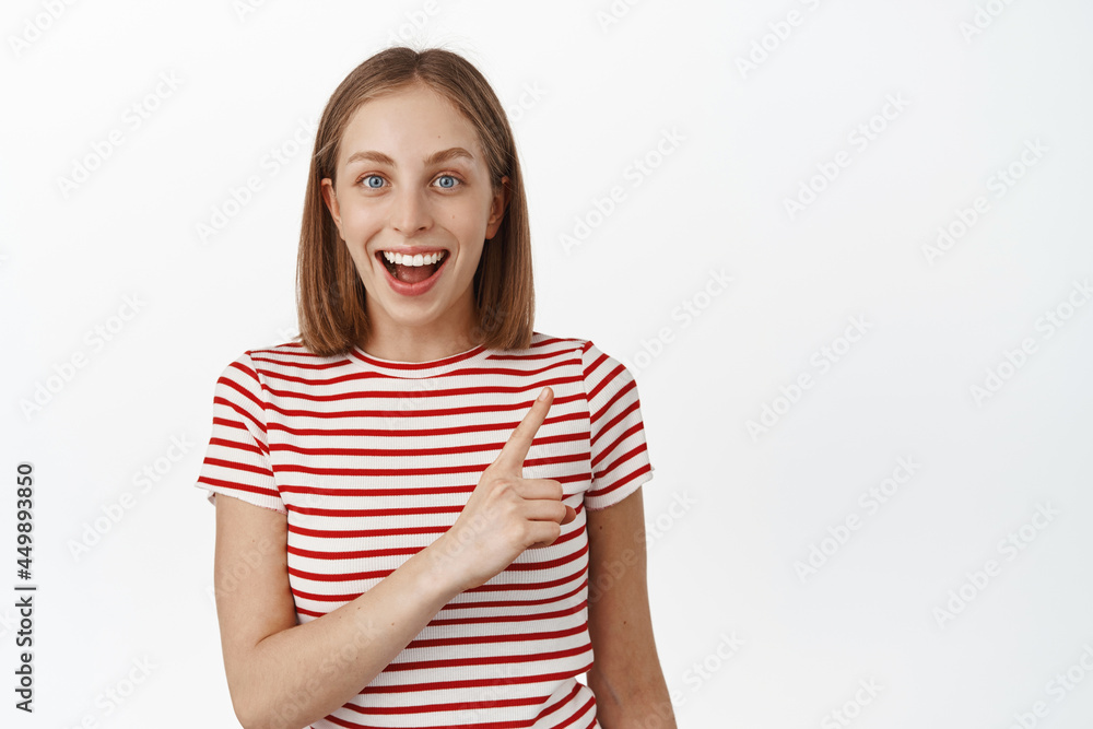 Wow look at that. Smiling excited girl with short fair hair, looking amused and pointing finger at upper right corner, laughing amazed, standing against white background Wow look at that. Smiling excited girl with short fair hair, looking amused and pointing finger at upper right corner, laughing amazed, standing against white background