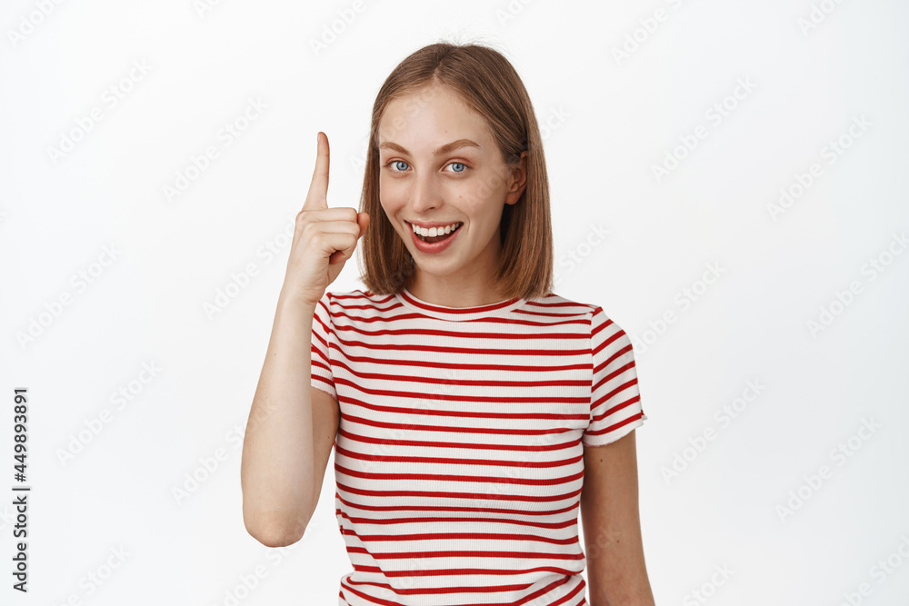 Portrait of pretty smiling female model with white smile teeth, pointing finger up and laughing, showing company logo, banner or sale promo deal, white background Portrait of pretty smiling female model with white smile teeth, pointing finger up and laughing, showing company logo, banner or sale promo deal, white background