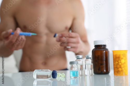 Man filling syringe at table indoors, focus on drugs. Doping concept