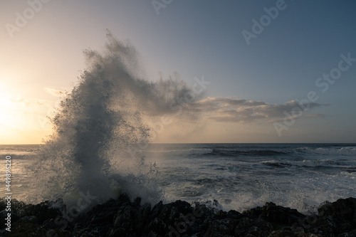 Wave crashing onto rocks at sunset
