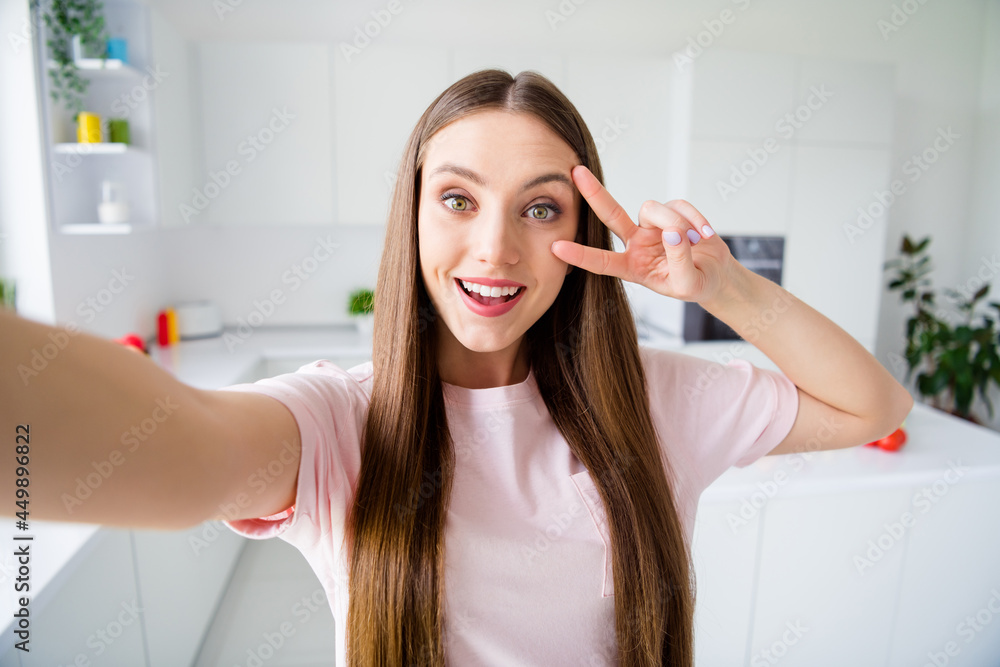 Photo portrait young woman smiling taking selfie in kitchen at home showing v-sign gesture Photo portrait young woman smiling taking selfie in kitchen at home showing v-sign gesture