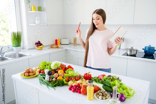 Portrait of attractive cheerful curious long-haired girl choosing fresh vegs vitamin salad at home light white kitchen indoors