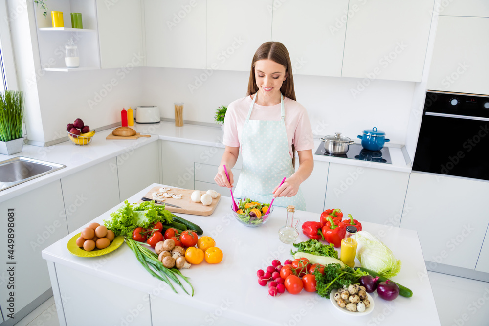 Portrait of attractive skilled girl cooking tasty yummy salad meal mixing ingredients in light white home kitchen indoors