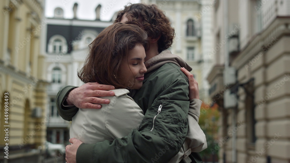 Fototapeta premium Lovely couple hugging on street. Happy girlfriend leaning to boyfriend outdoor.