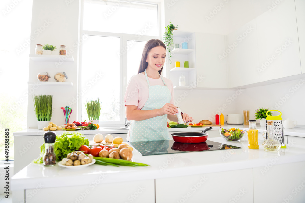 Portrait of attractive cheerful girl adding spices frying omelet cuisine at home light white kitchen indoors