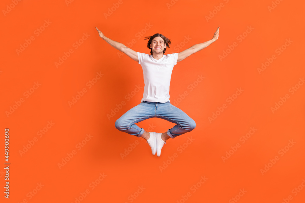 Full body photo of cheerful young happy man jump up raise hands enjoy smile isolated on orange color background Full body photo of cheerful young happy man jump up raise hands enjoy smile isolated on orange color background